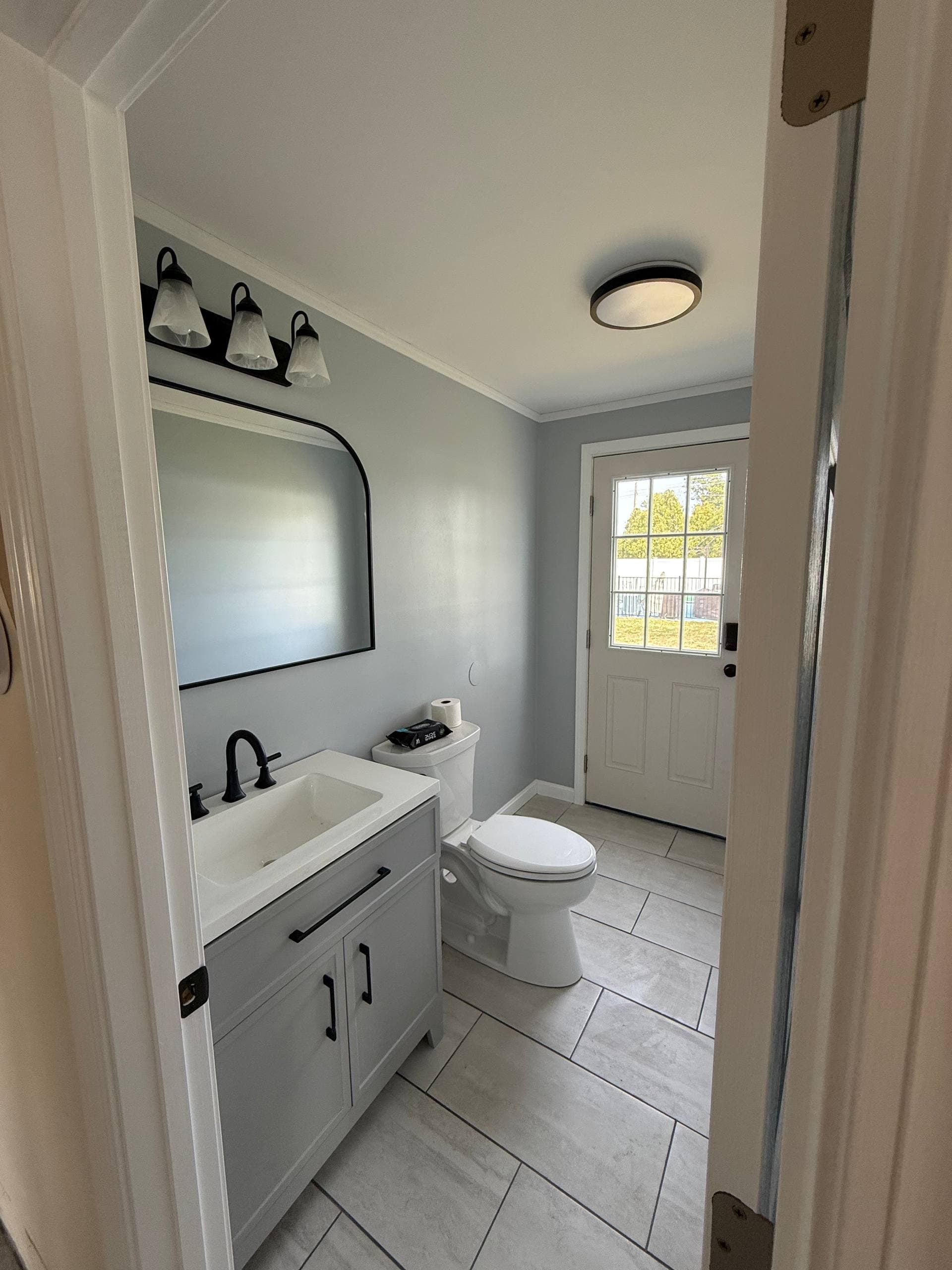 Renovated bathroom with new shaker vanity, arched mirror, and new exterior door leading to the backyard