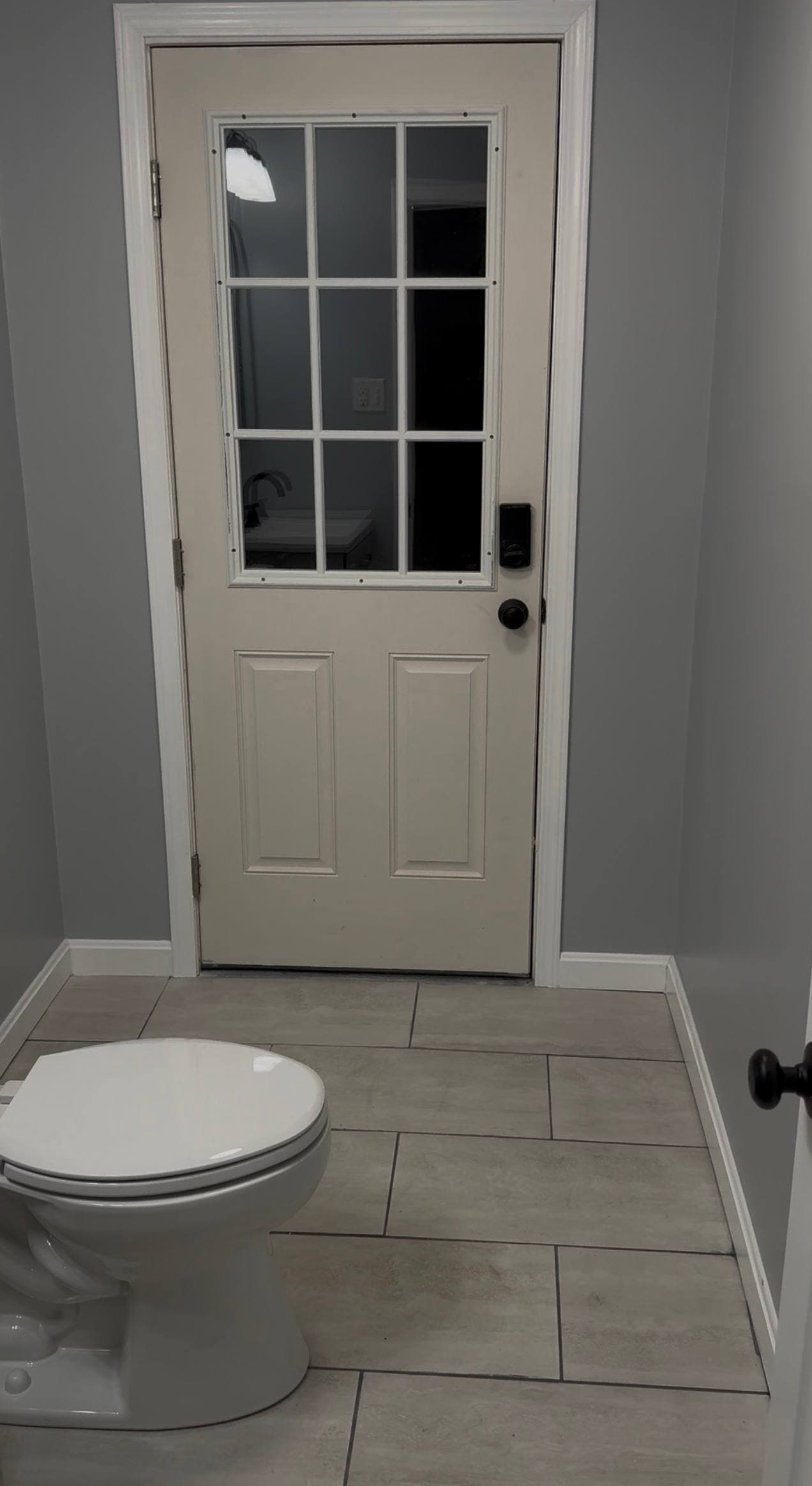 New 9-lite exterior door with centered toilet and marble-look floor tile