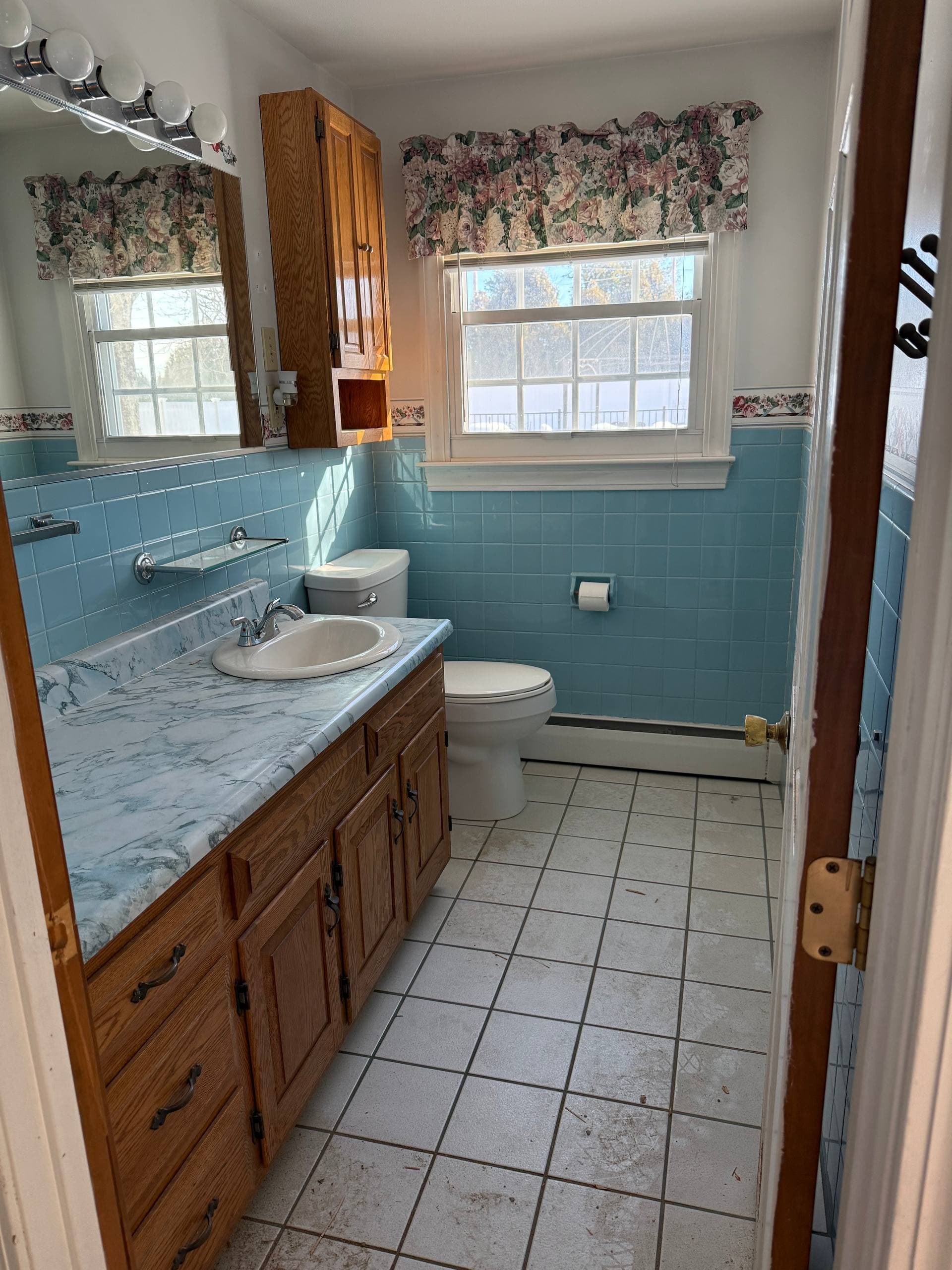 Original bathroom with blue wall tile, oak vanity, and toilet in the back corner by the window
