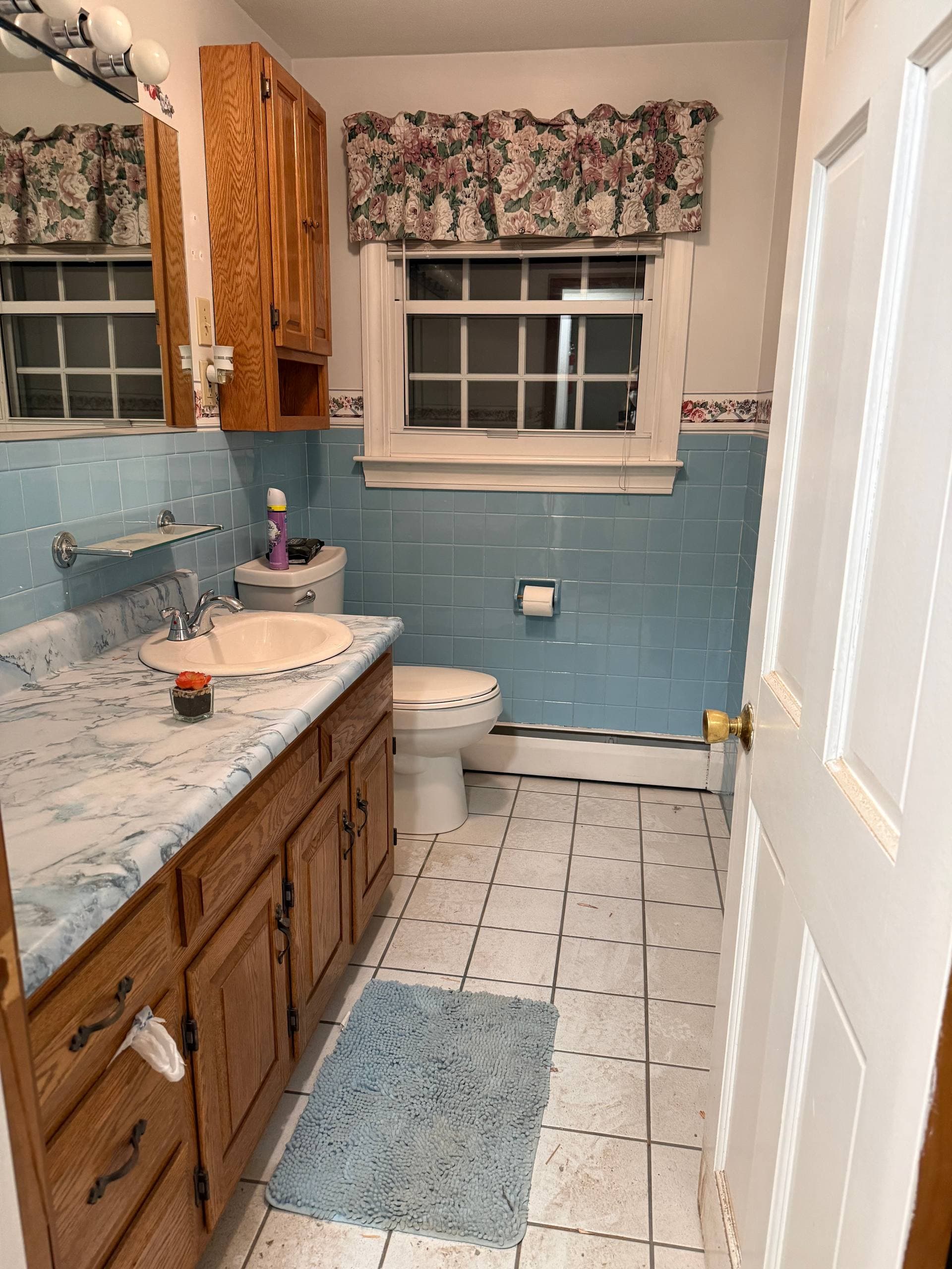 Original bathroom showing dated blue tile, oak cabinetry, and window where the new exterior door was installed