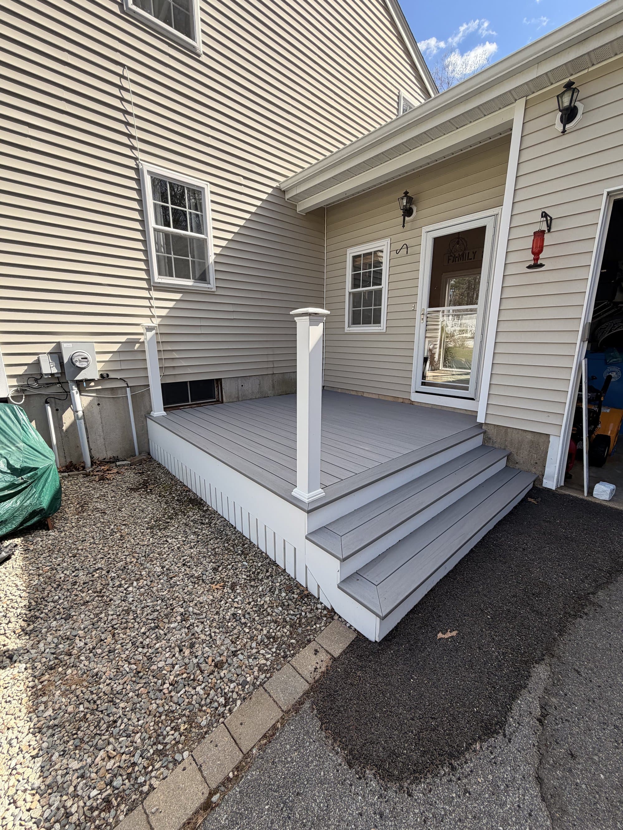 Full daylight view of the completed deck, white vinyl skirting, and wide stairs down to the driveway