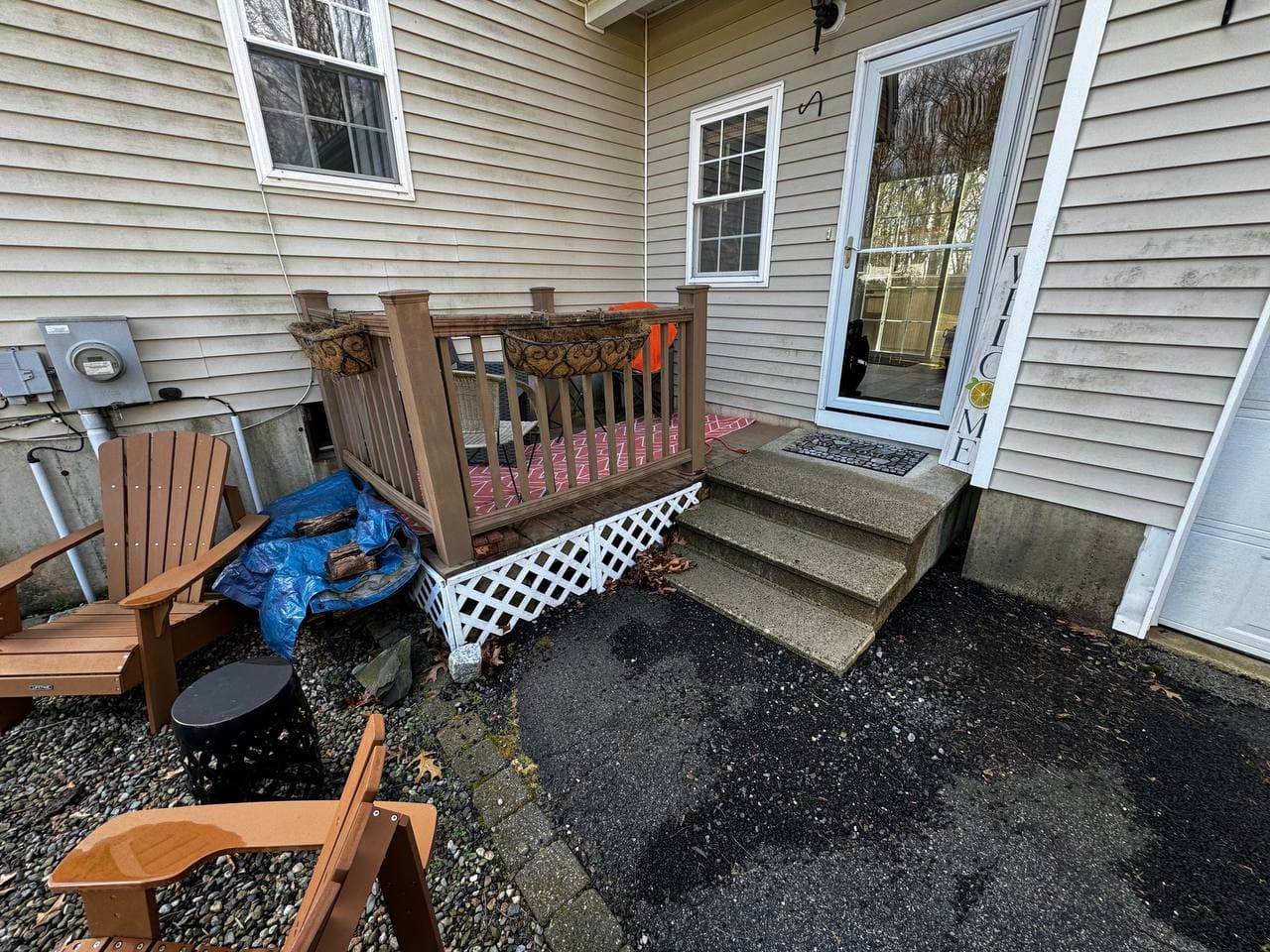 Original side entry with a small wooden landing, brown railings, and welcome mat on the concrete steps before the rebuild