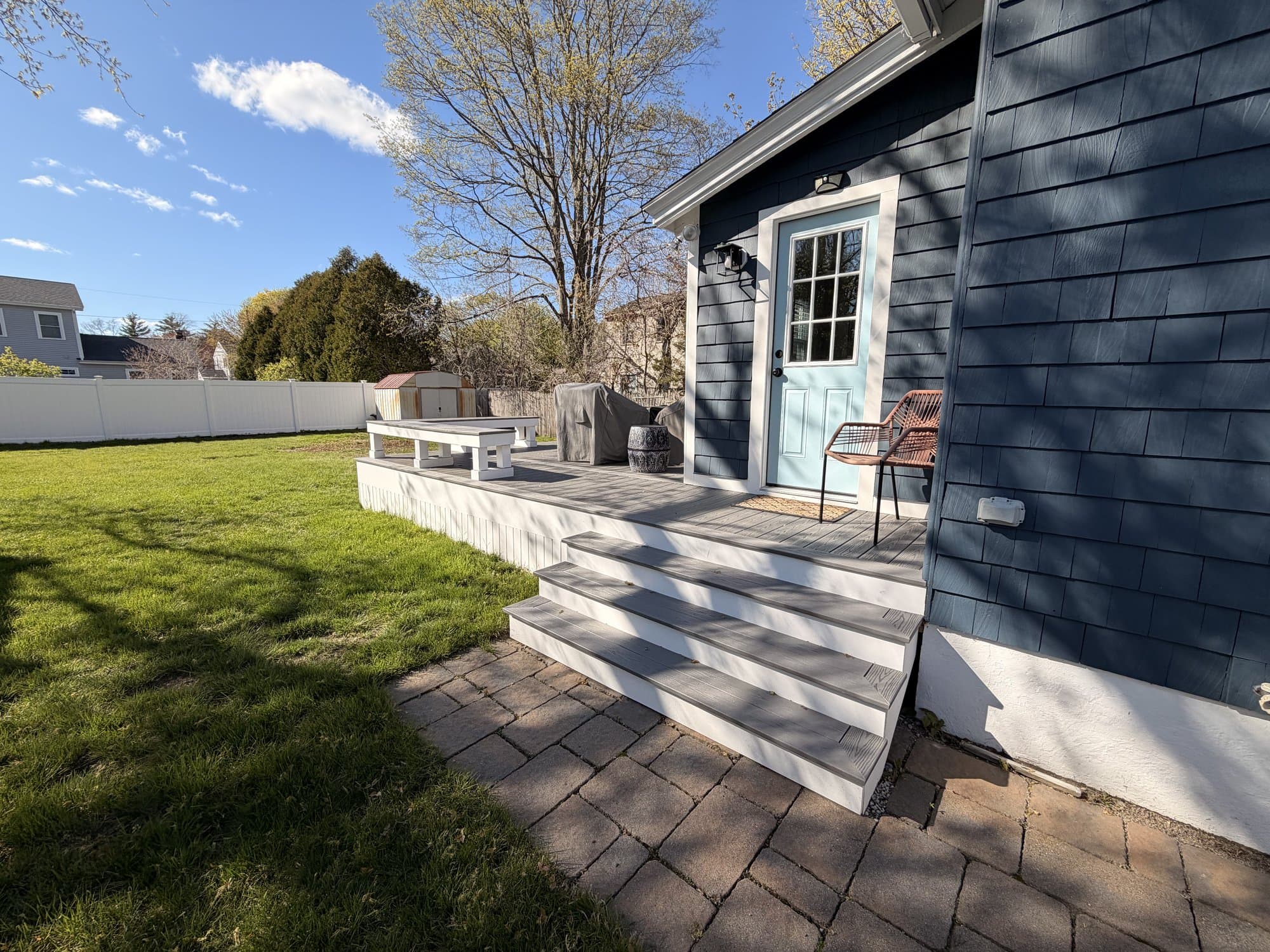 Finished composite deck with bench seating beside a cottage's blue back door, golden afternoon light