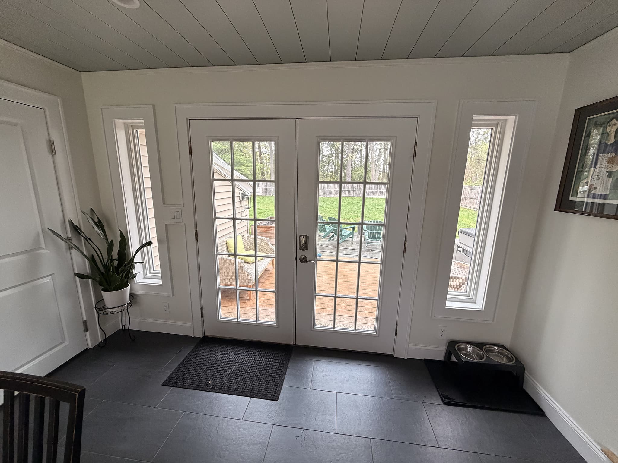 Relocated French doors with new sidelight windows leading to the back deck, framed by shiplap ceiling and slate-look tile floor