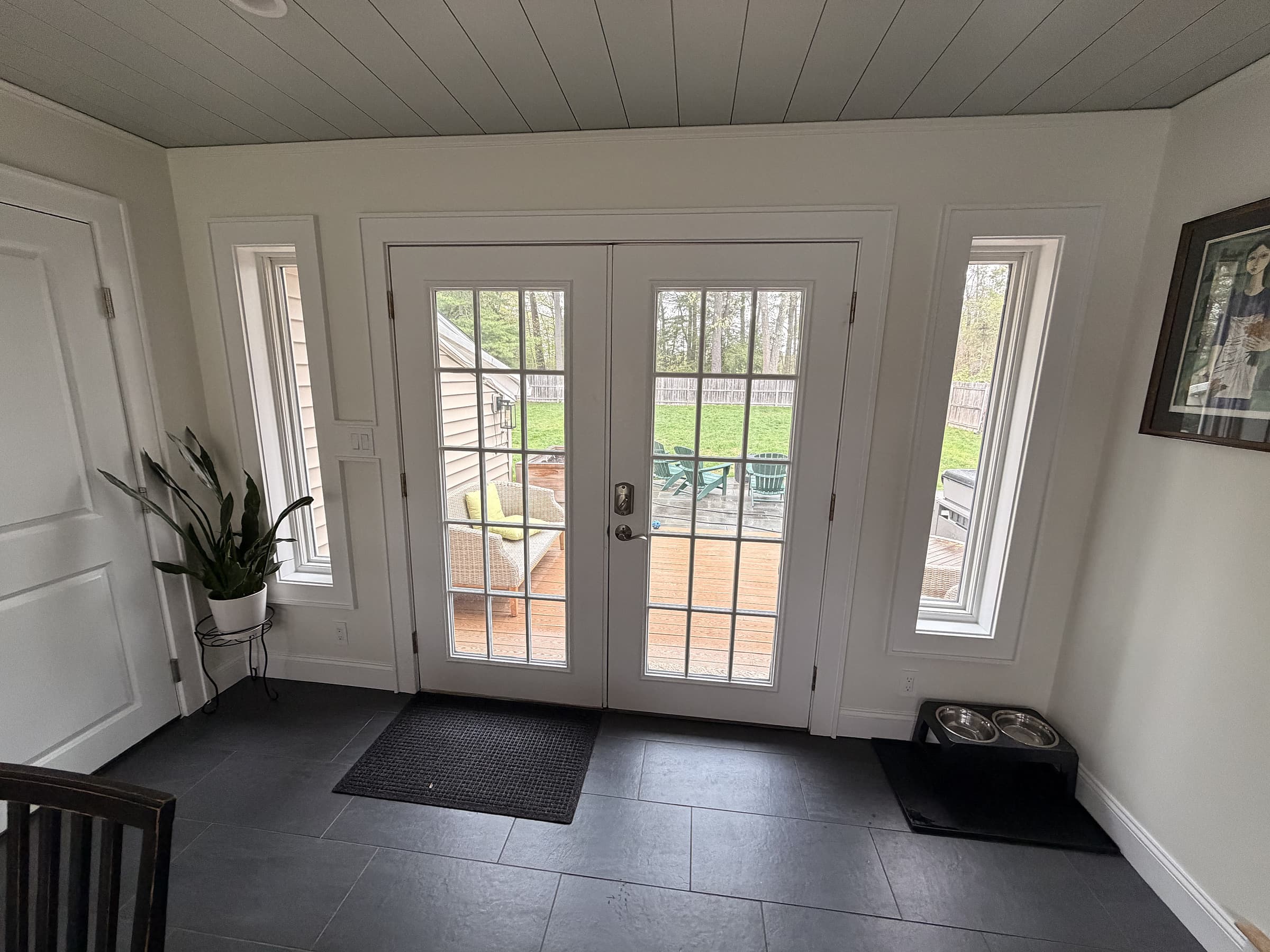 Relocated French doors with new sidelight windows leading to the back deck, framed by shiplap ceiling and slate-look tile floor