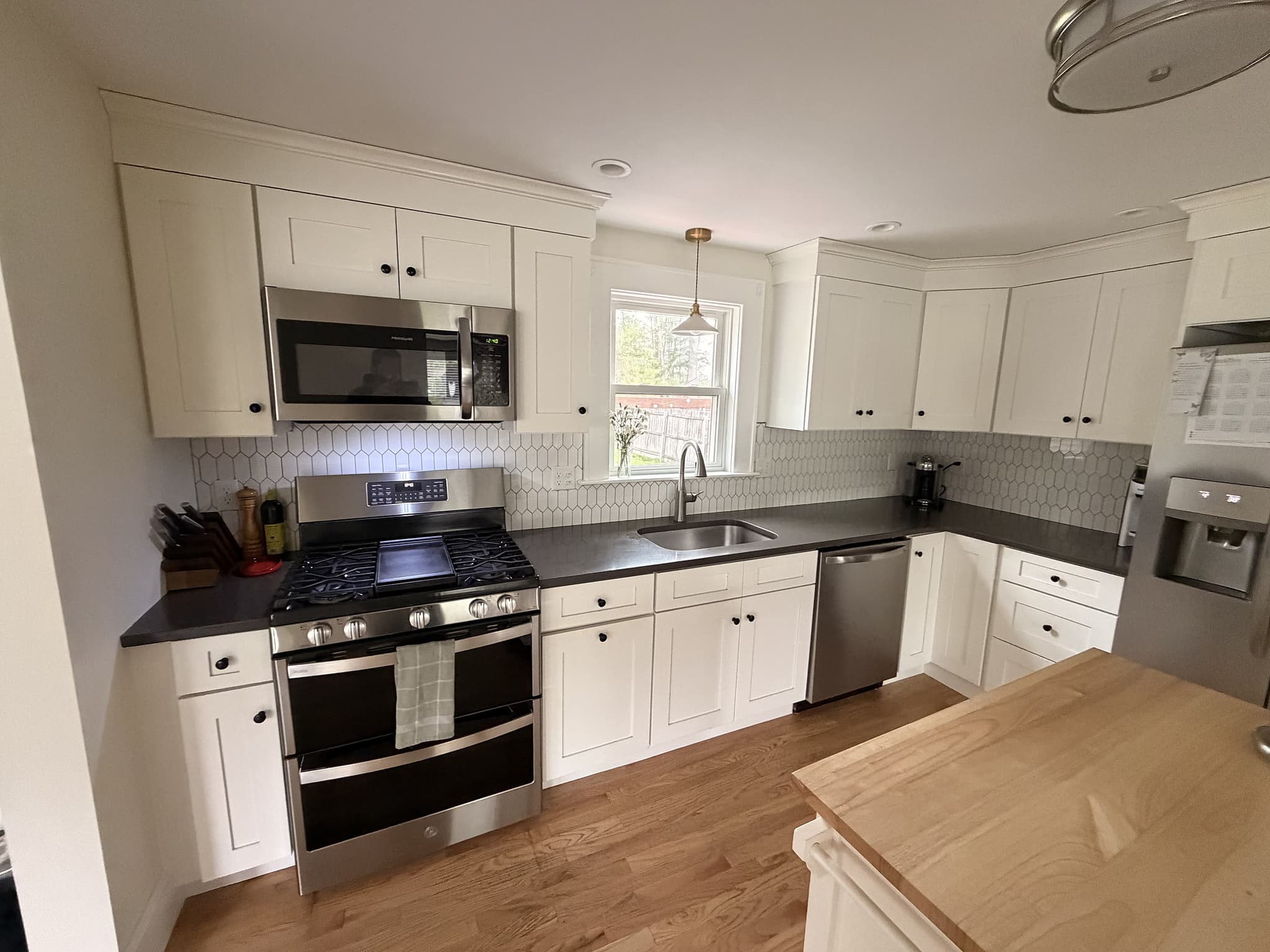 Refreshed kitchen with new hex-tile backsplash, white shaker cabinets, dark quartz counters, and stainless gas range