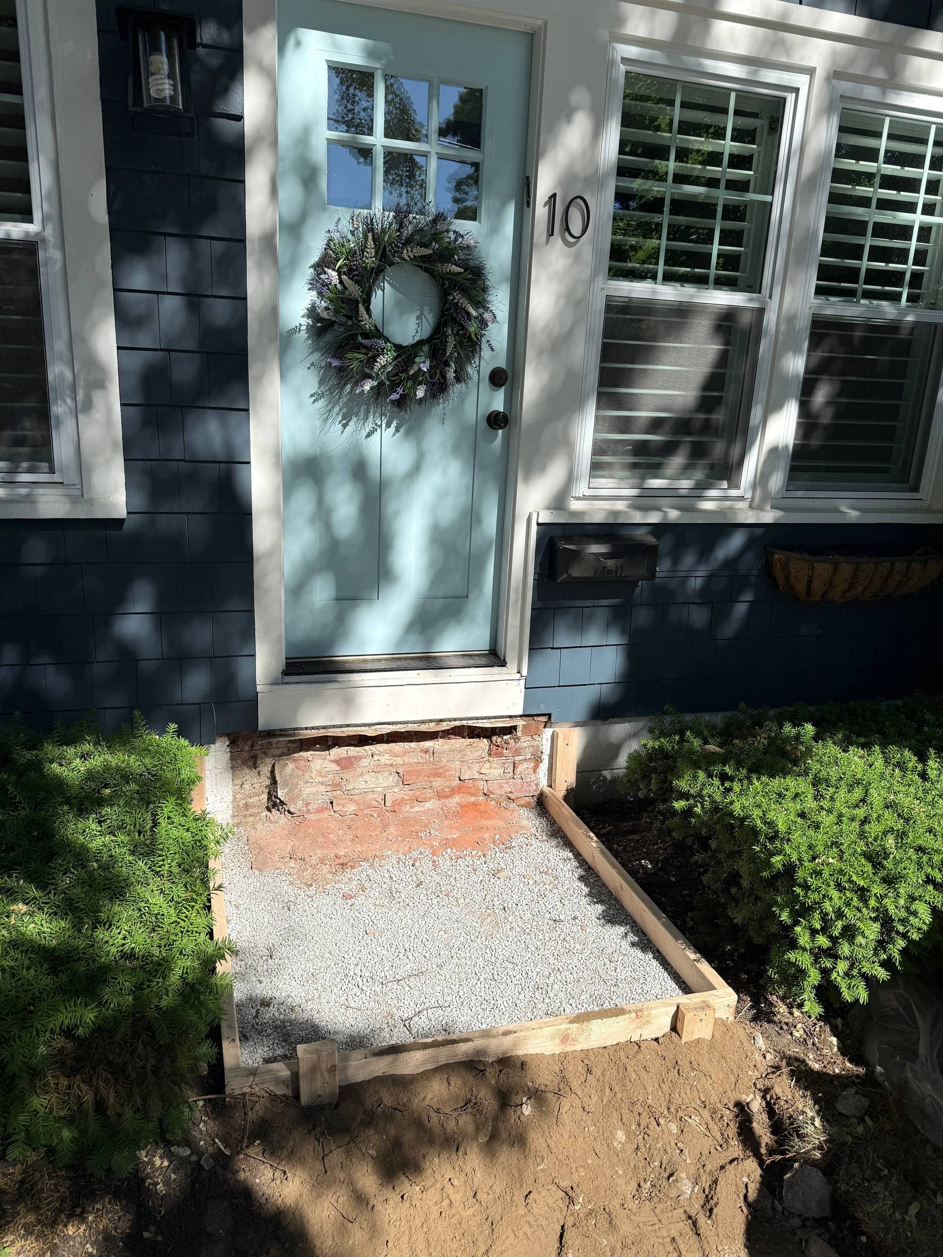 Original steps removed and the exposed brick foundation, with a framed washed-stone base prepped at the doorway