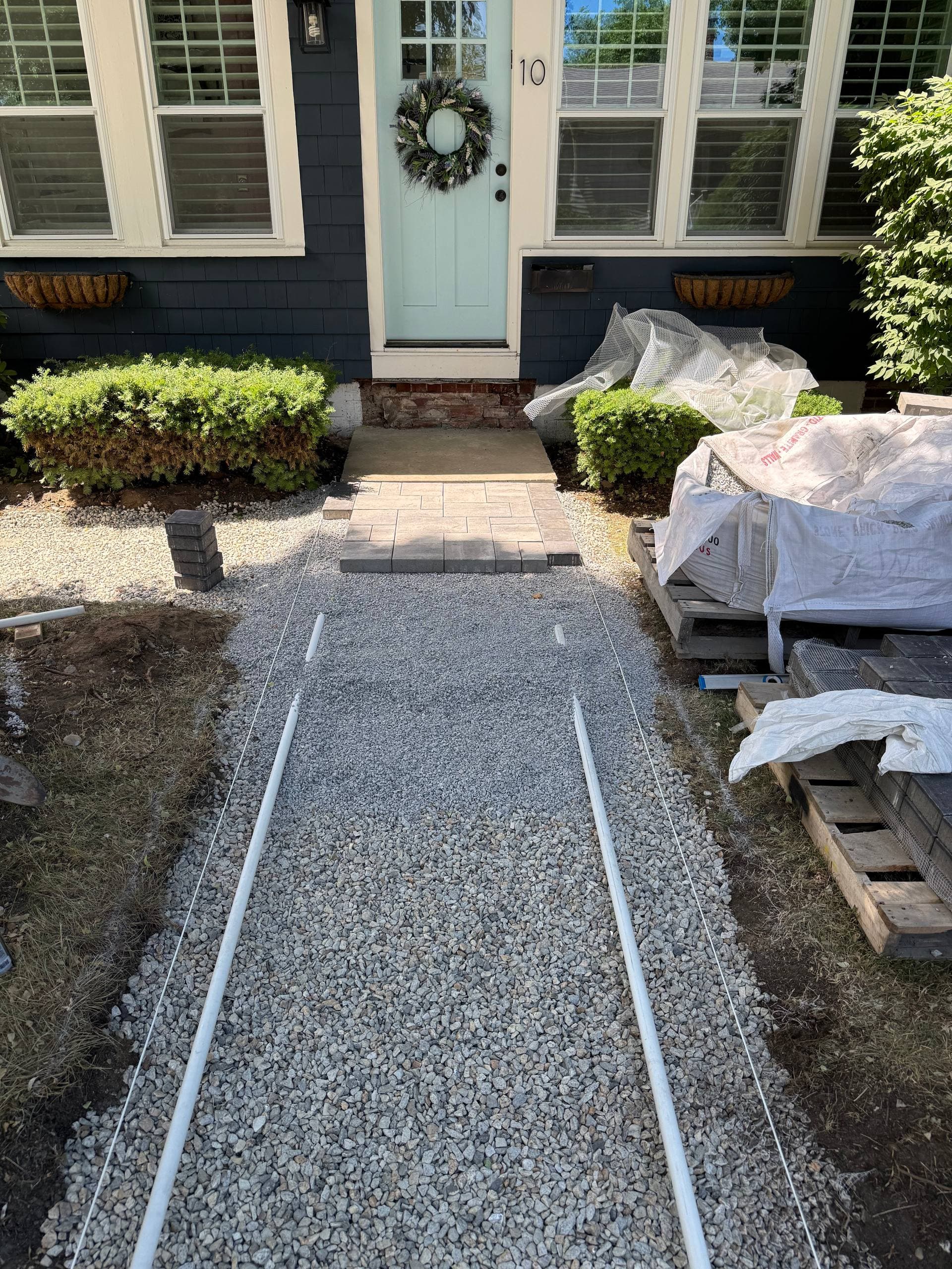 Compacted stone base with string lines set and the first pavers being laid toward the front door