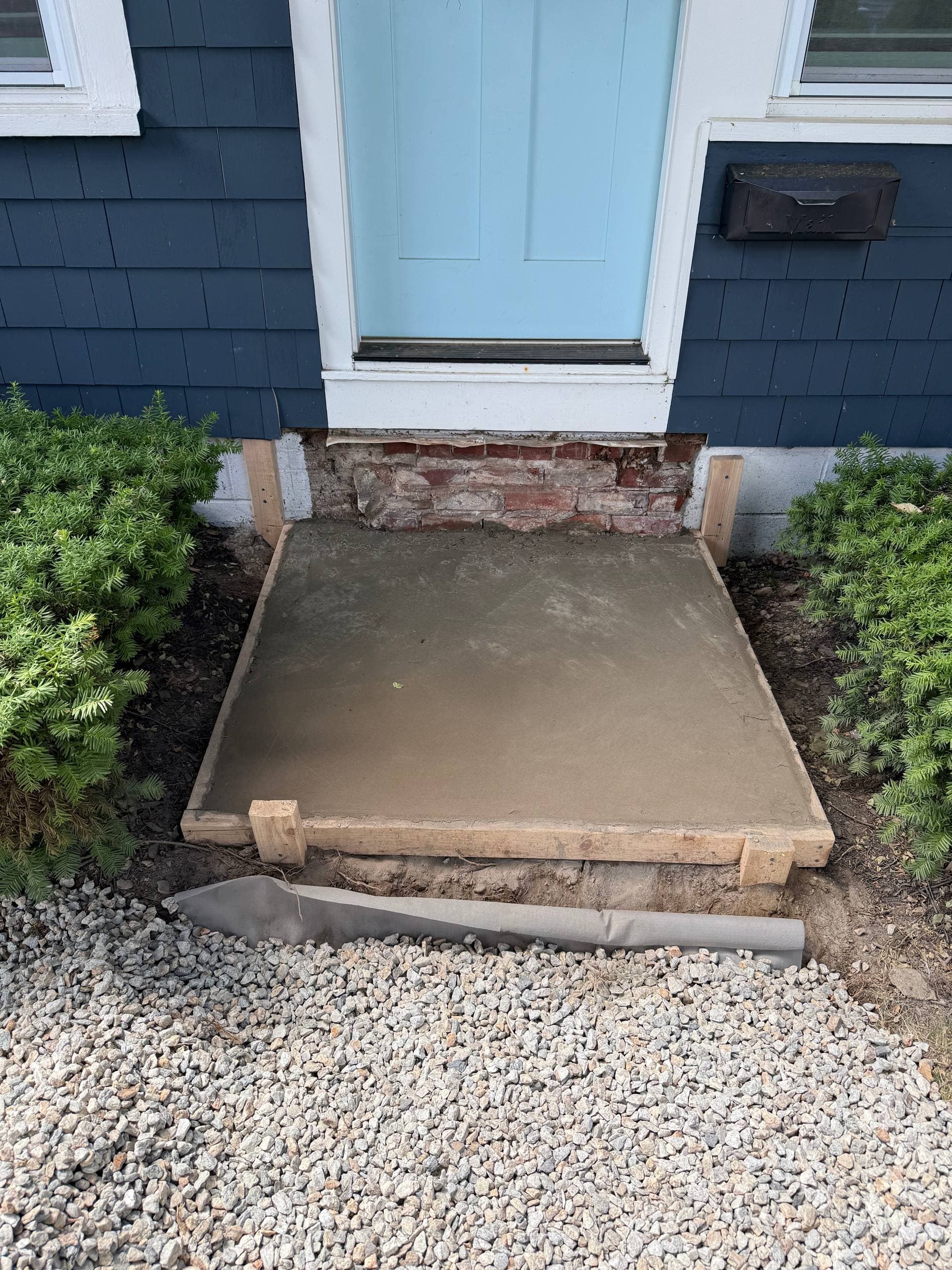 Freshly poured concrete pad curing in its wood forms at the doorway, ready for the granite treads