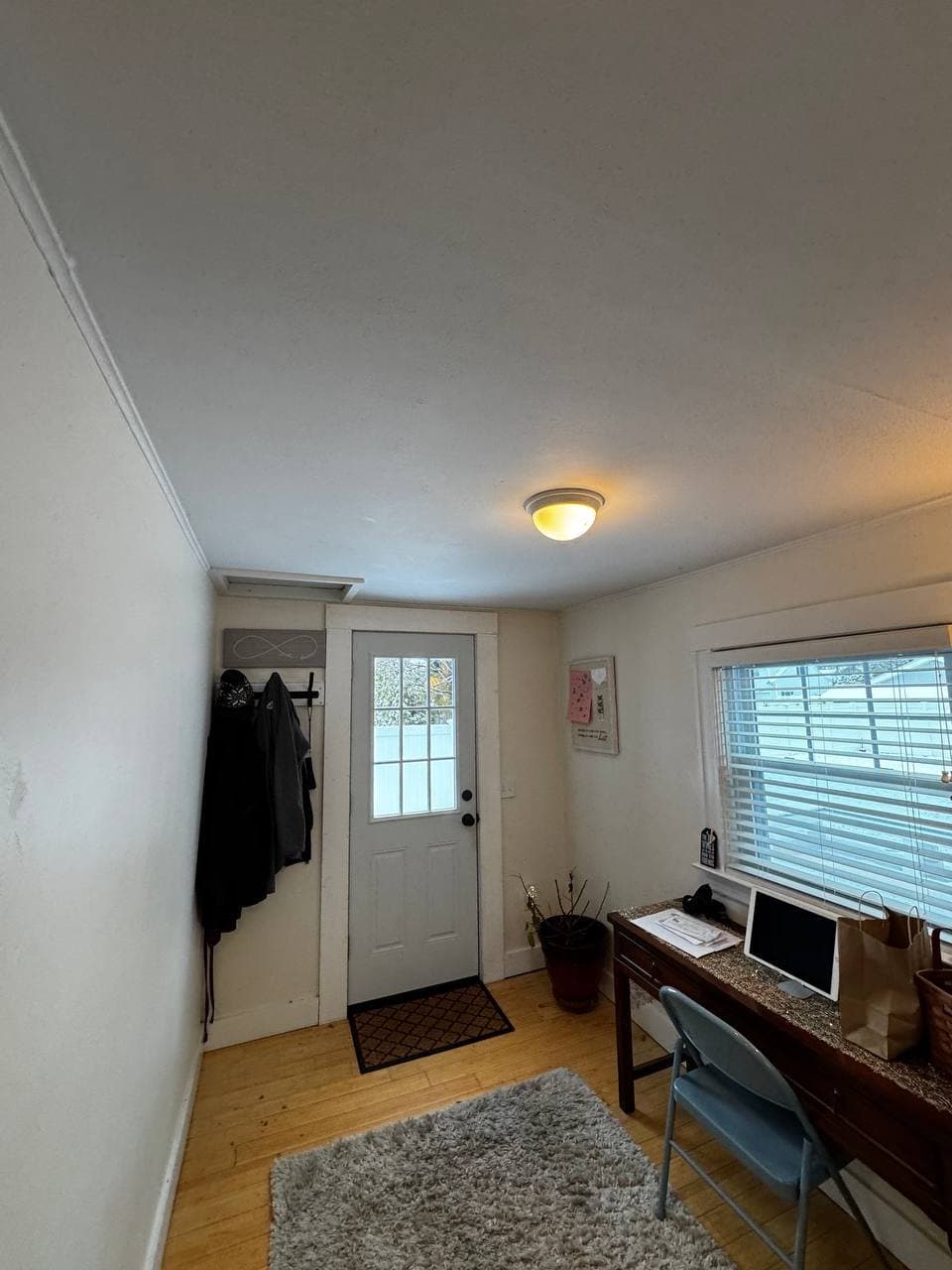 Original mudroom before renovation — dated door, basic coat hooks, and old desk against the window wall