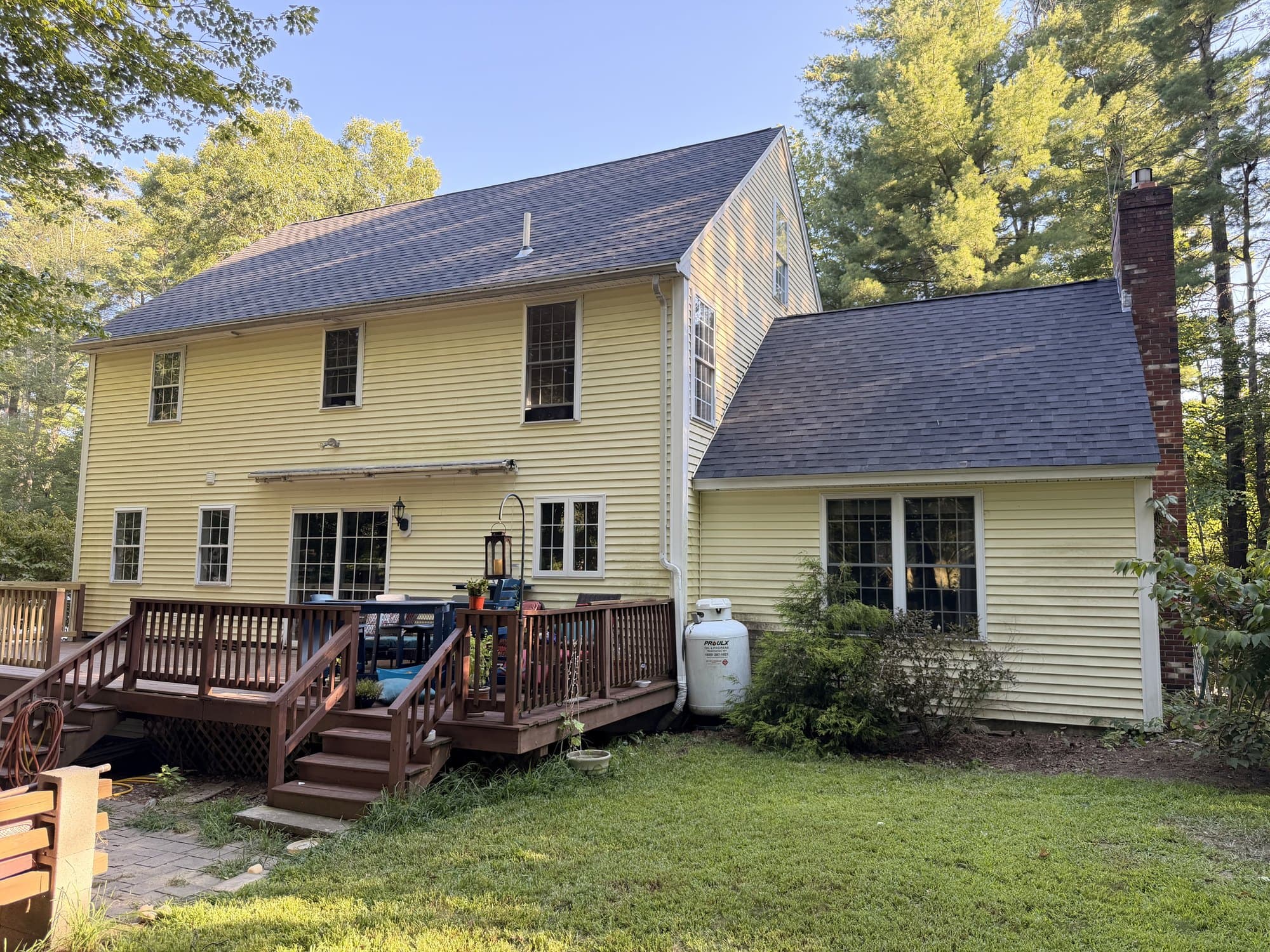 Rear and side view of the finished roof, showing new Dual Black shingles across the main roof, the rear ell, and around the brick chimney