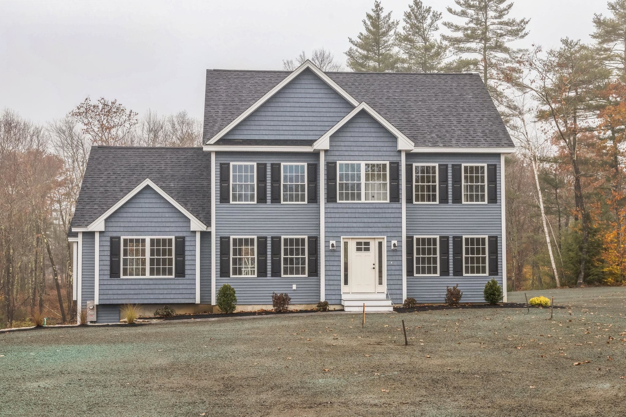 Front exterior of a custom-built colonial with navy siding, white trim, and attached two-car garage