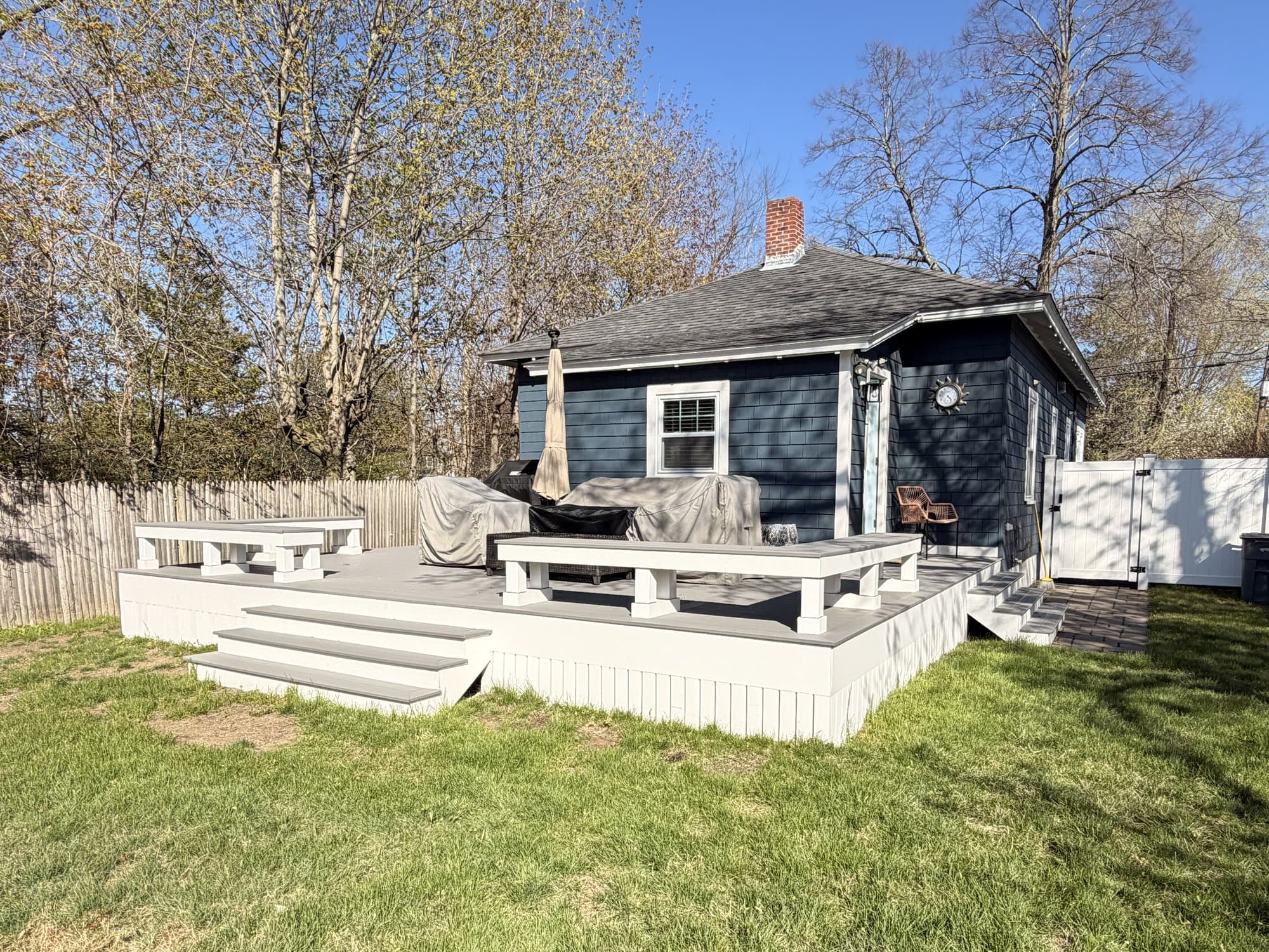 Wide golden-hour view of a ground-level composite deck wrapping the back of a cottage
